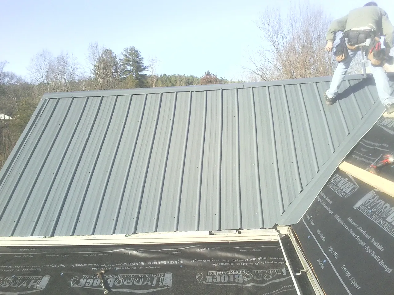 Crew installing dark green standing seam panels over synthetic underlayment in Elkhorn City