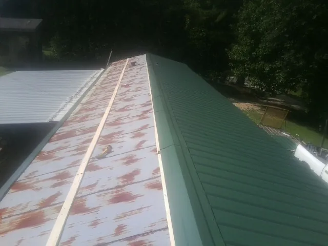 Old rusted panels beside newly installed green metal roofing — Wind Damage Roof Repair by Roofing Brothers in Elkhorn City