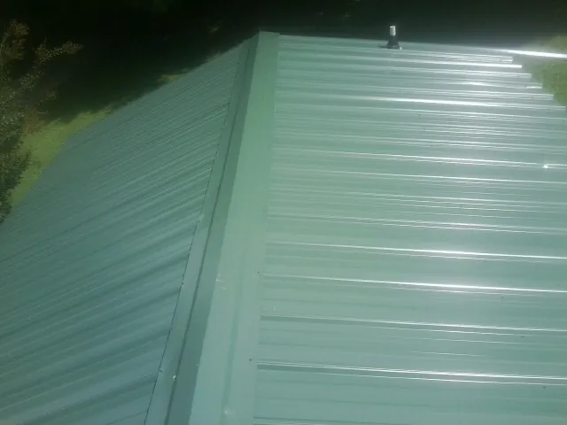 New green metal panels meeting at the ridge of a roof — Flat Roof Repair work by our crew in Elkhorn City