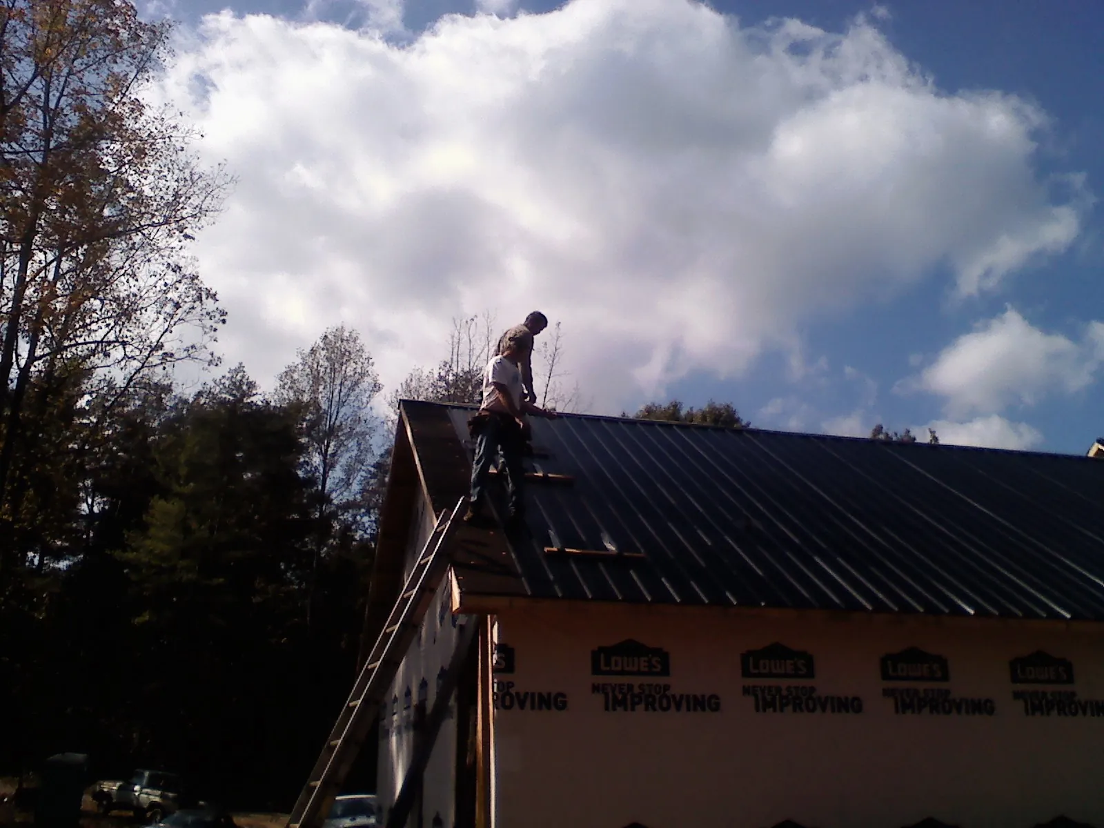 Roofer fastening dark metal panels high against a cloudy sky, from a Roof Inspection job in Elkhorn City