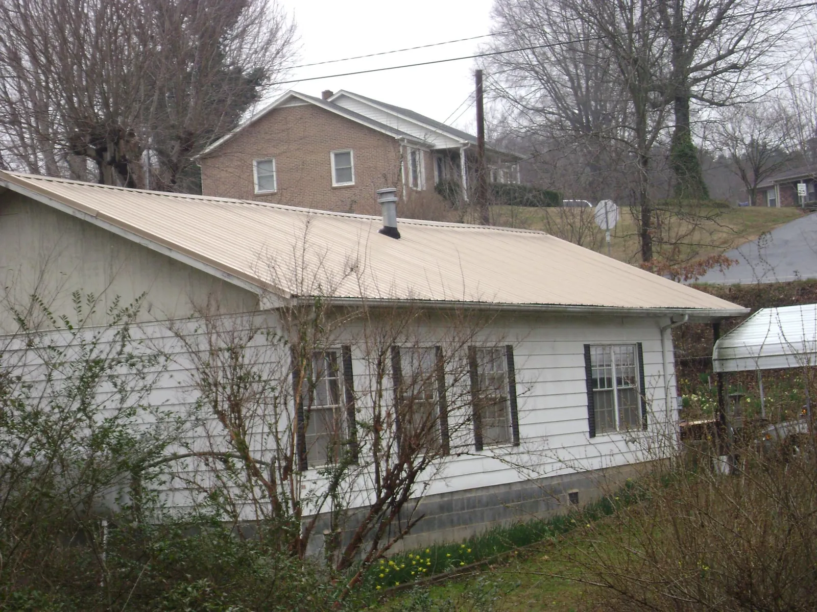 Tan metal roof on a white sided house set into a hillside — Commercial Roofing by Roofing Brothers in Elkhorn City